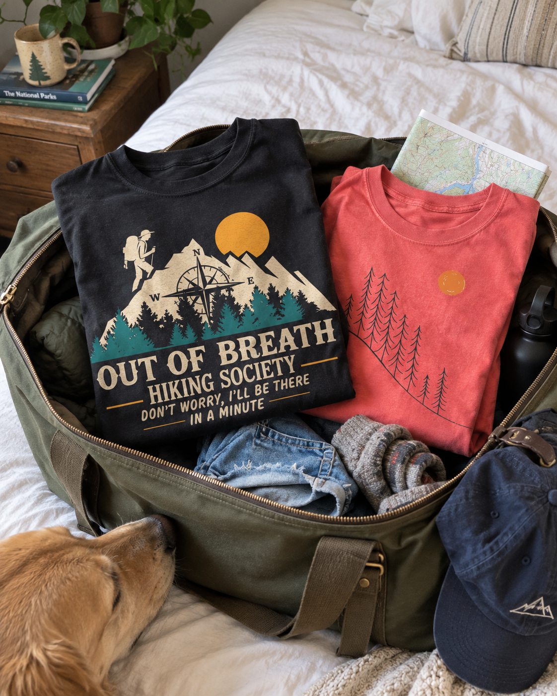 Out Of Breath and Sunrise Pines tees packed in an olive weekend bag beside a curious dog.