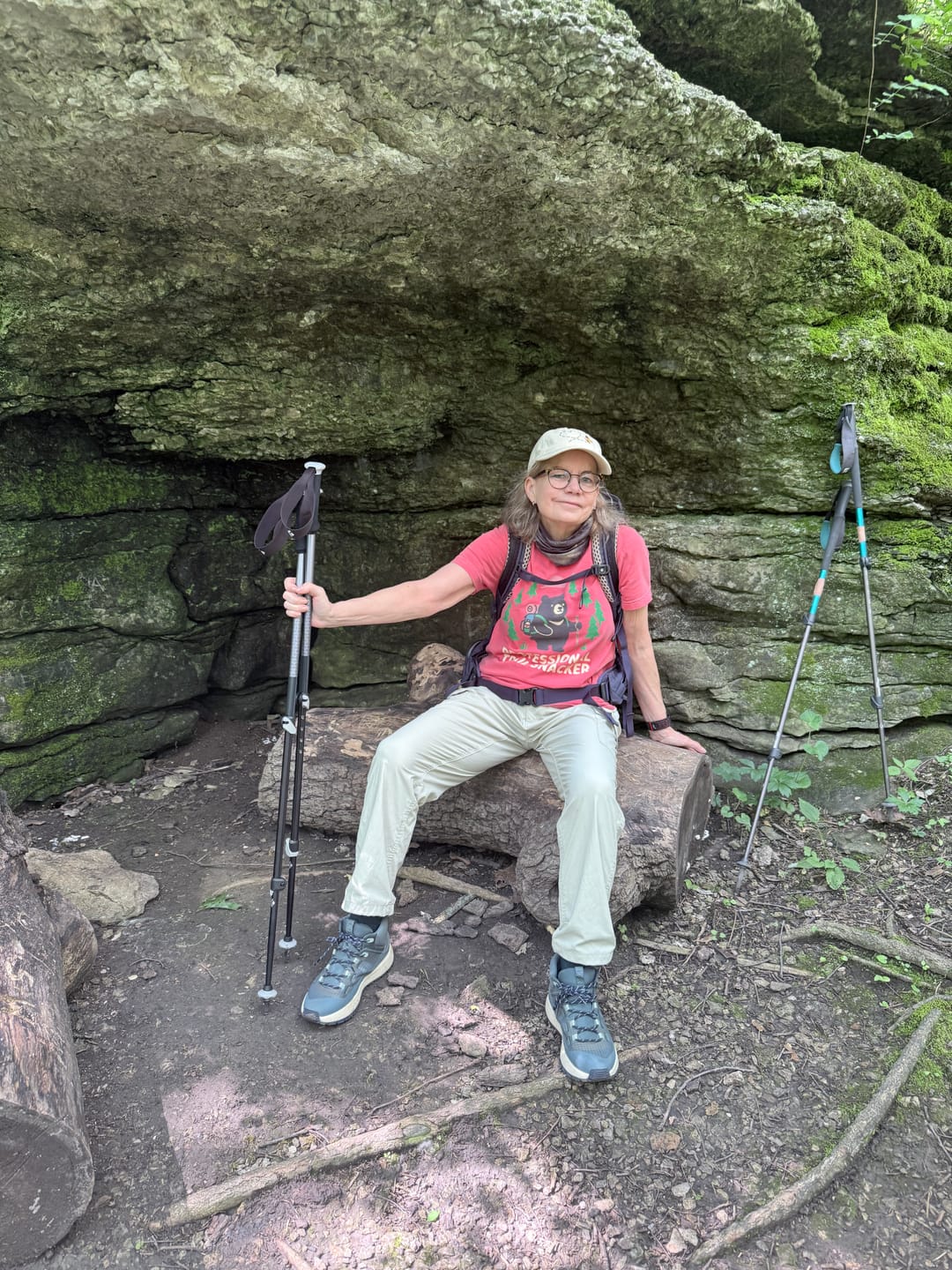 Donna smiling on a hike in her Pro Snacker tee, seated beside her hiking poles